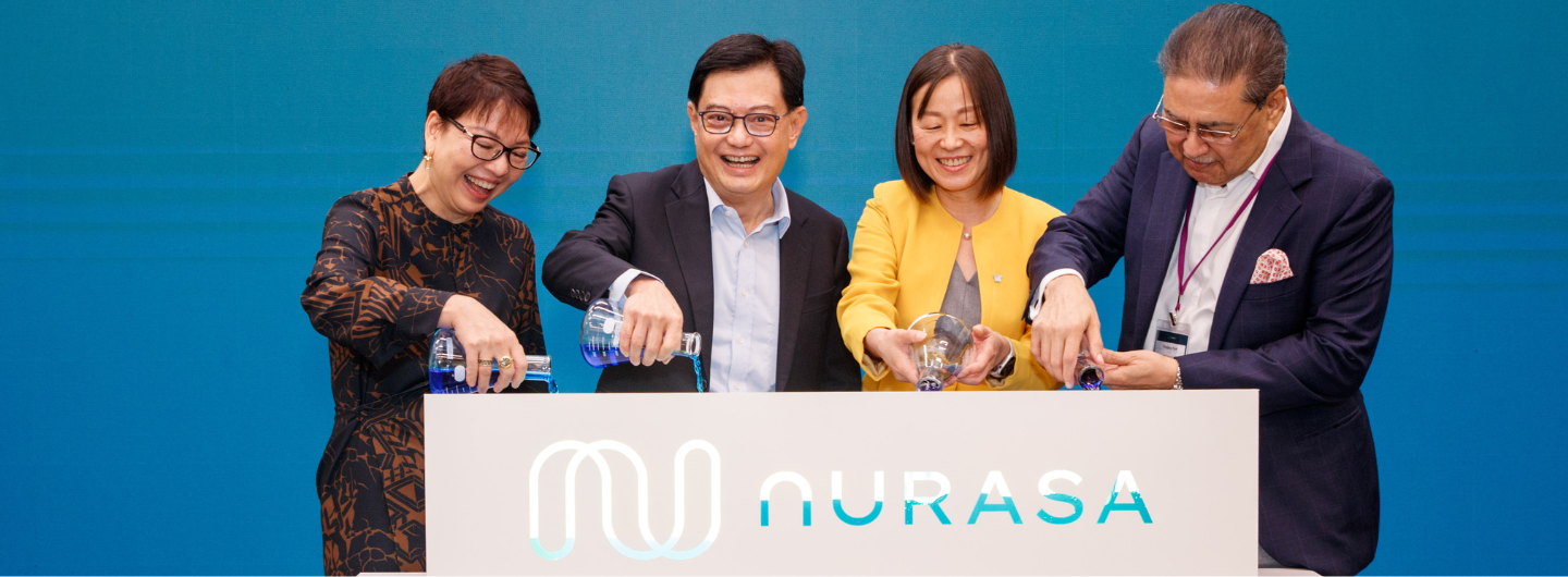 Four people in business attire pour blue liquid into glassware over an "Aurasa" logo.